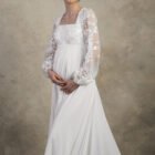 Front view of a maternity gown with an embroidered bodice and long lace sleeves.