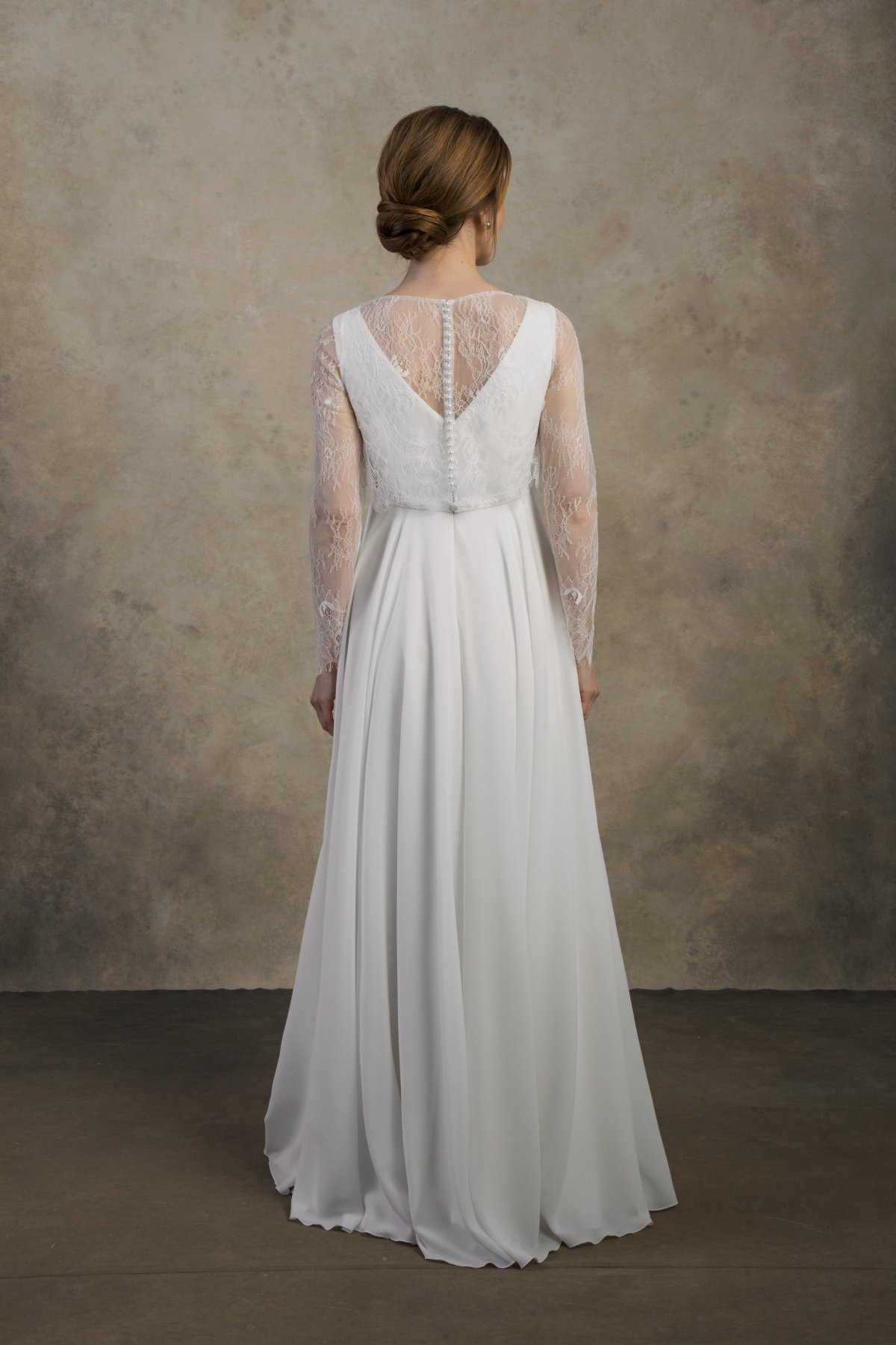 Back view of a maternity gown with lace sleeves, illusion back, and a flowing chiffon skirt.