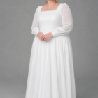 Elegant plus size wedding dress featuring a square neckline, sheer long sleeves and a softly flowing tea-length skirt. The silhouette highlights a defined waist and graceful movement, creating a refined and modern bridal look.