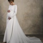 Side view of a long-sleeve maternity gown with a smooth fitted bodice and long elegant train.