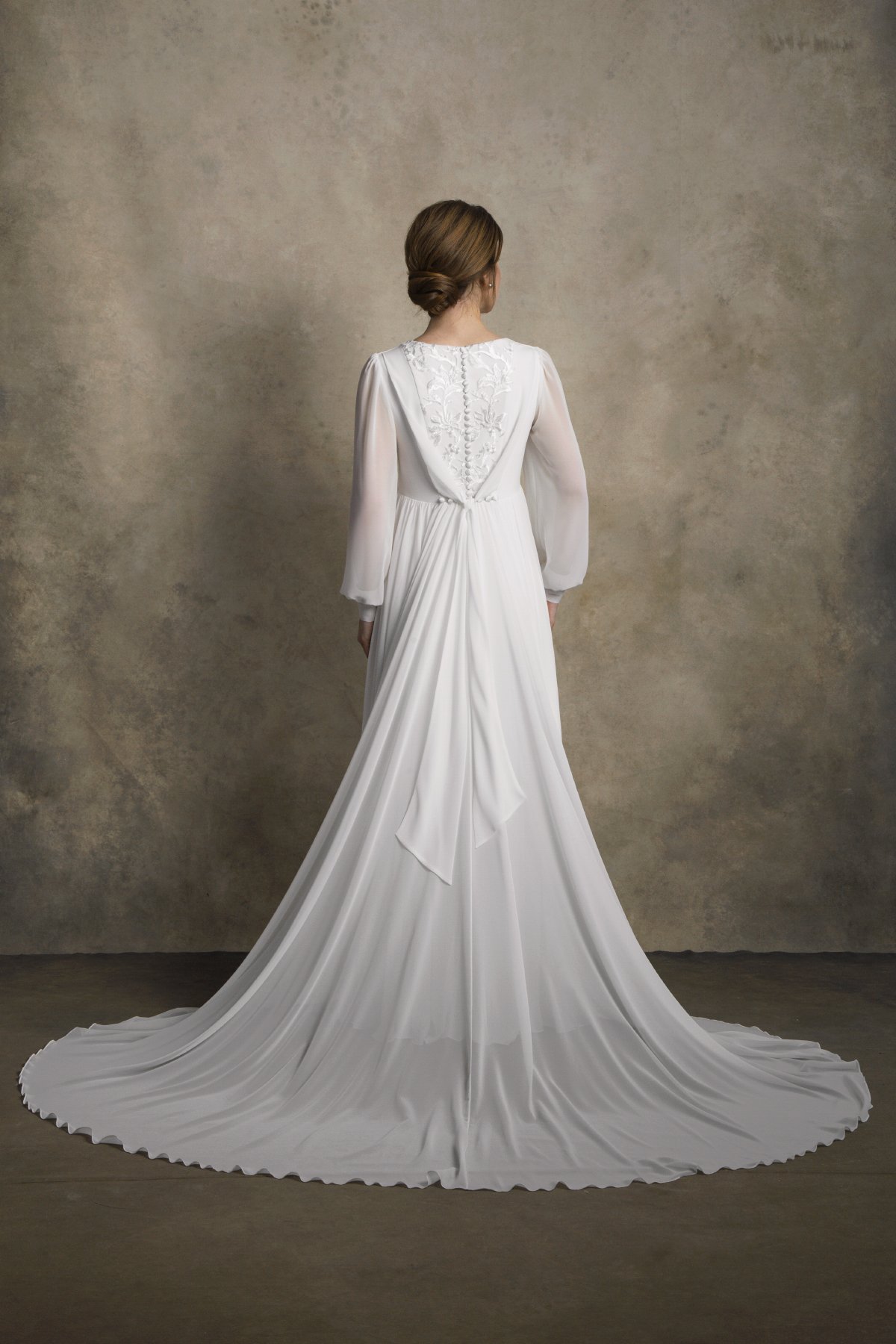 Full back view of a maternity chiffon gown with embroidered detail and a long draped train.