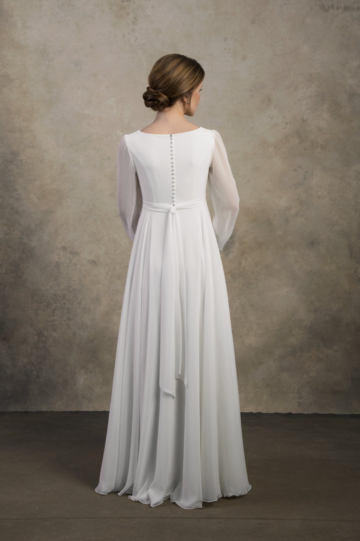 Back view of a maternity chiffon gown with long sheer sleeves and covered buttons.