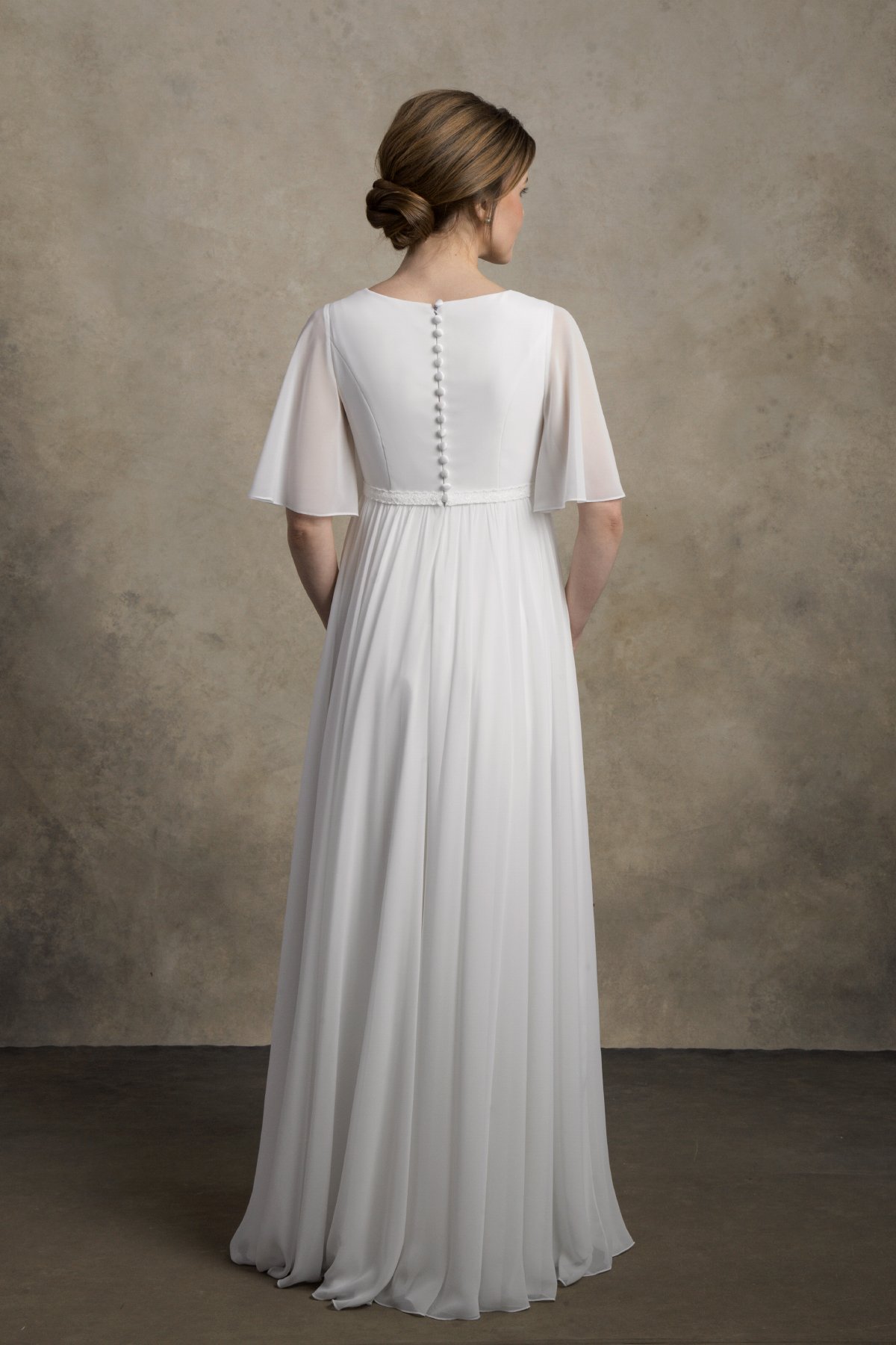 Back view of a maternity chiffon gown with flutter sleeves and covered buttons.