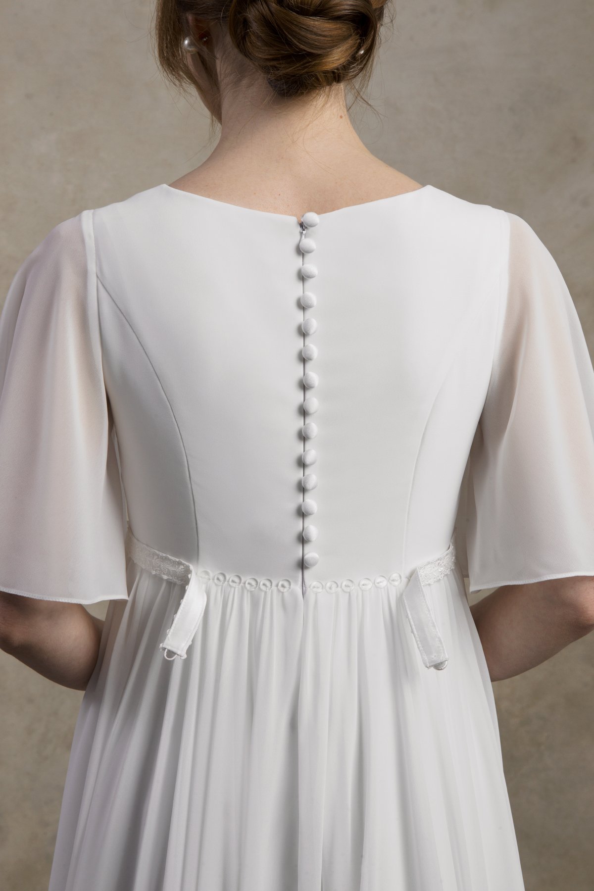 Close-up of the back of a maternity chiffon gown with flutter sleeves, covered buttons, and soft waist ties.
