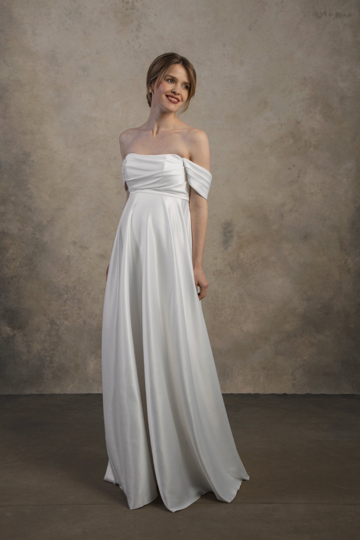 Front view of an off-the-shoulder maternity gown with a draped bodice and flowing skirt.