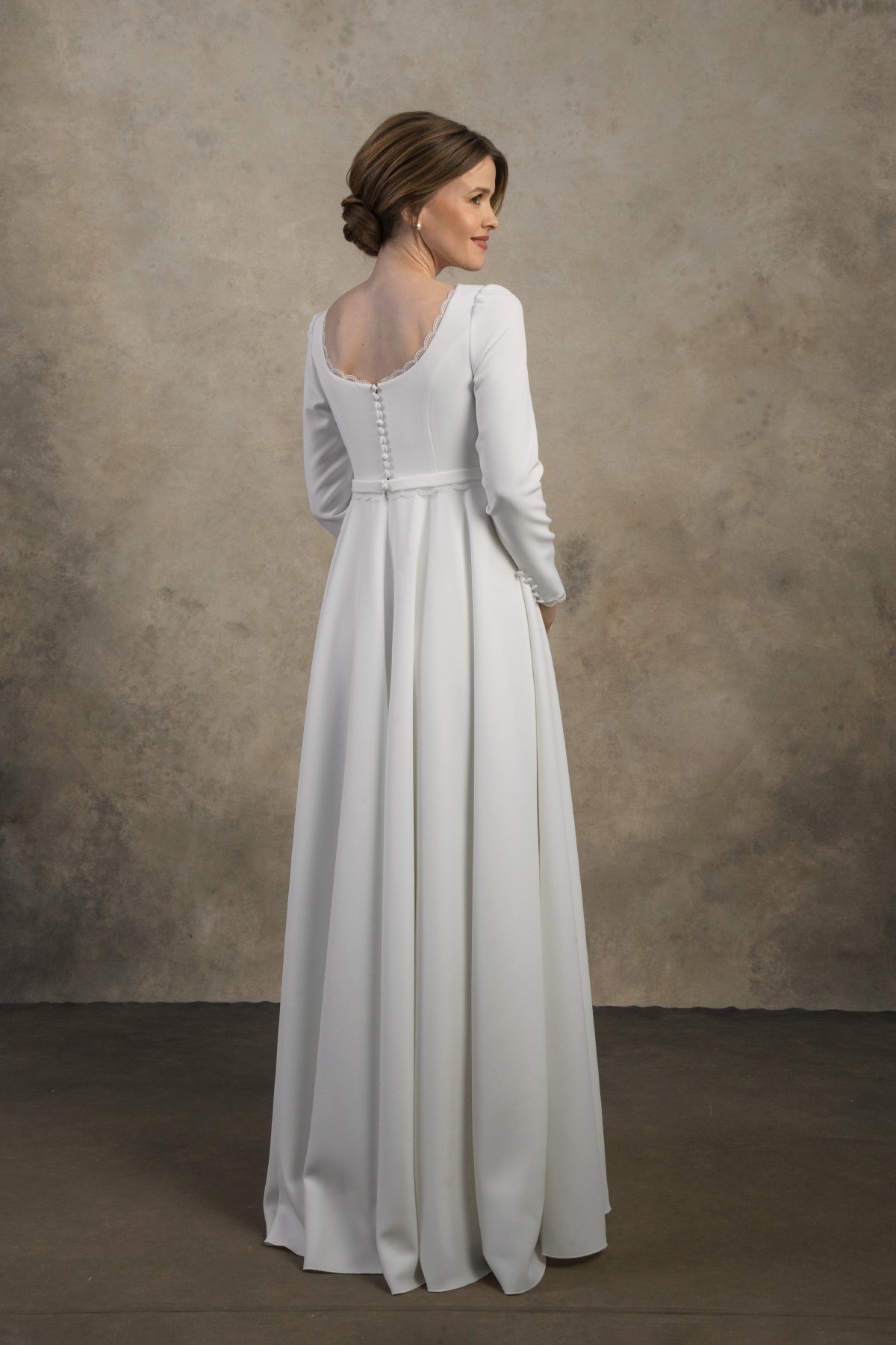 Side-back view of a long-sleeve maternity gown with a structured bodice and flowing skirt.