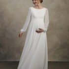 Maternity gown with long sheer sleeves, a clean neckline, and a softly flowing skirt.