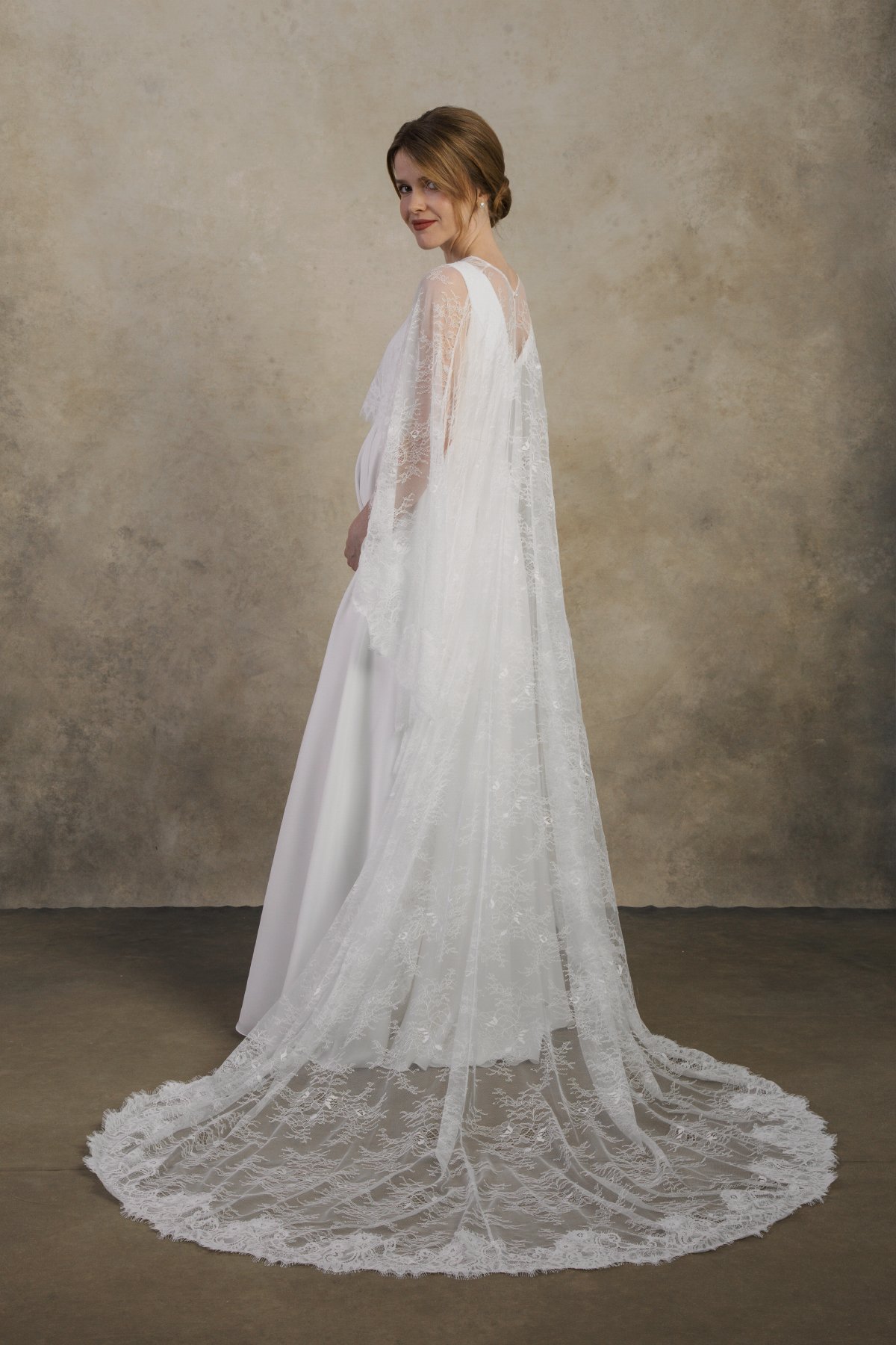 Back-side view of a maternity gown with a full-length lace cape and scalloped train.
