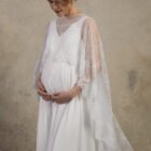 Front view of a maternity gown with a lace cape and V-neckline.
